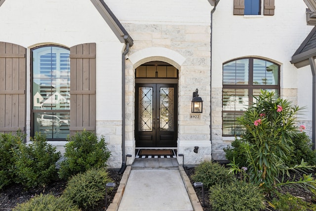 view of exterior entry featuring stone siding, brick siding, and french doors