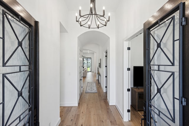 entrance foyer with arched walkways, a towering ceiling, light wood-style flooring, and baseboards