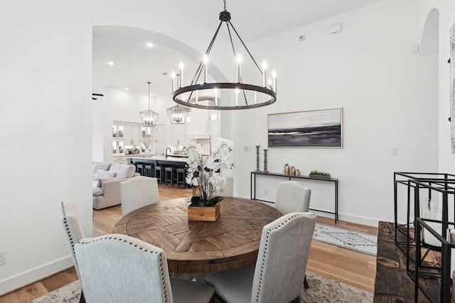 dining area with arched walkways, light wood-style flooring, baseboards, and an inviting chandelier