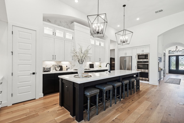 kitchen with a center island with sink, glass insert cabinets, light countertops, and appliances with stainless steel finishes