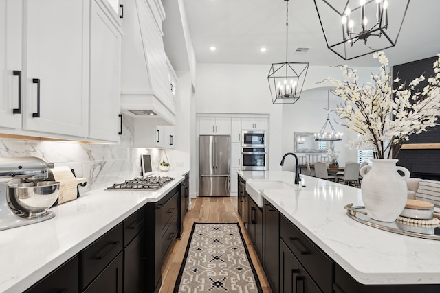 kitchen with white cabinets, an island with sink, stainless steel appliances, pendant lighting, and a sink