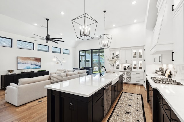 kitchen featuring dark cabinets, stainless steel appliances, a sink, open floor plan, and an island with sink