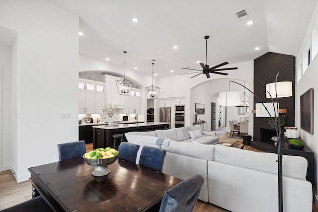 living room featuring light wood finished floors, visible vents, arched walkways, high vaulted ceiling, and recessed lighting