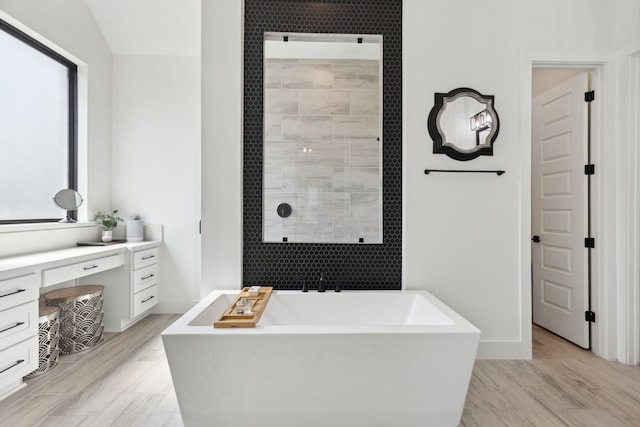 full bath with a soaking tub, vanity, wood finished floors, tiled shower, and baseboards