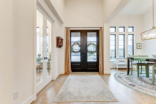 foyer entrance with a notable chandelier, french doors, a high ceiling, and light wood-style floors