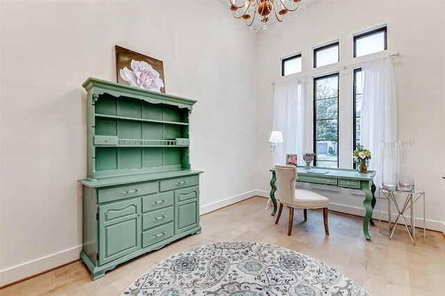 office space featuring light wood-style floors, a high ceiling, a notable chandelier, and baseboards