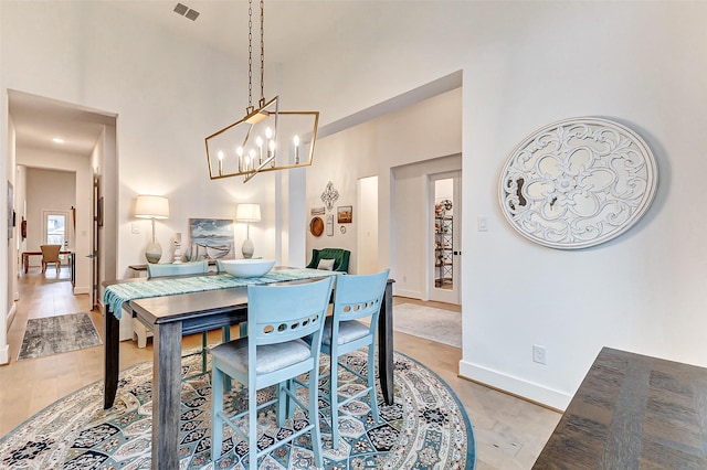 dining area featuring a towering ceiling, light wood-style flooring, visible vents, and baseboards