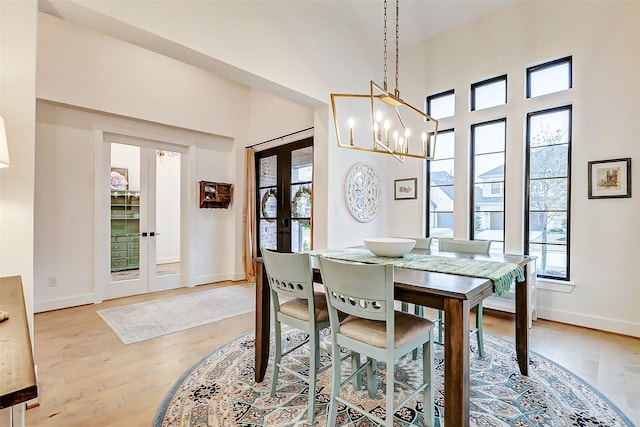 dining area with light wood-type flooring, french doors, a notable chandelier, and baseboards