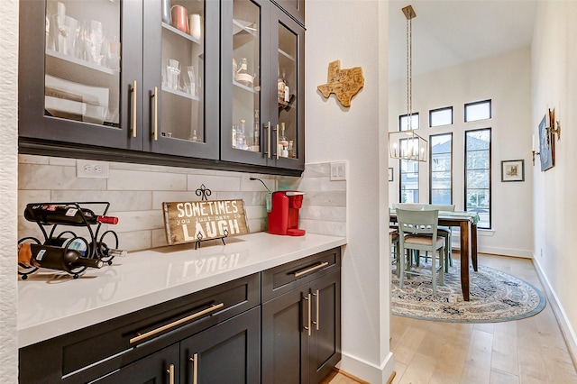 bar with tasteful backsplash, baseboards, light wood-style flooring, hanging light fixtures, and a chandelier