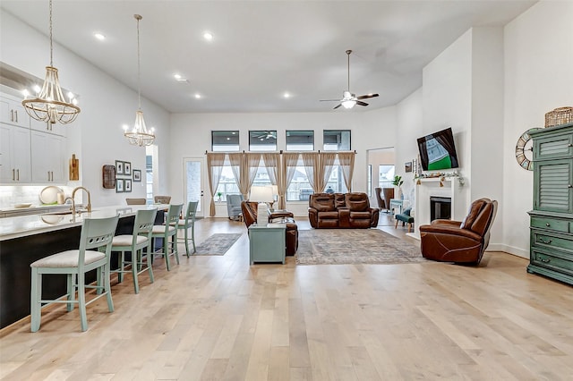 living area featuring a fireplace, recessed lighting, light wood-style flooring, a towering ceiling, and ceiling fan with notable chandelier