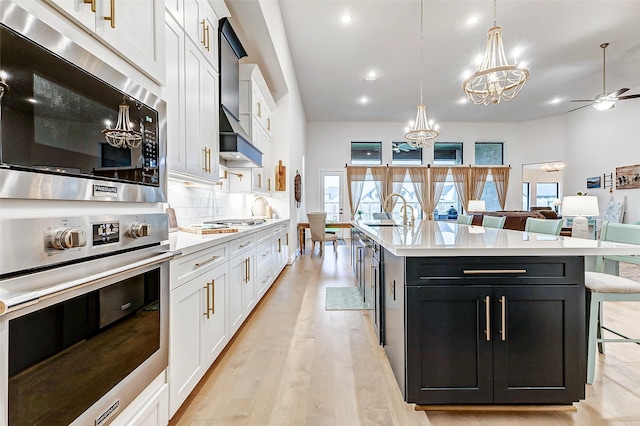 kitchen featuring appliances with stainless steel finishes, white cabinets, light countertops, and an island with sink