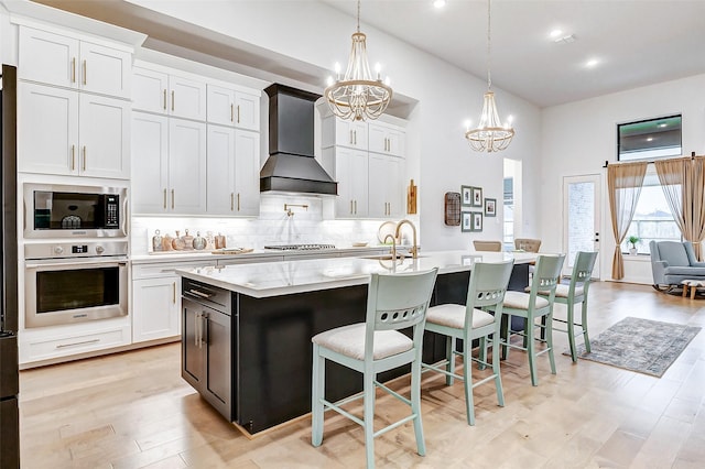 kitchen with stainless steel appliances, white cabinets, and premium range hood