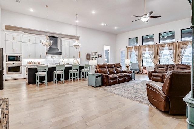 living area with recessed lighting, a high ceiling, light wood finished floors, and ceiling fan with notable chandelier