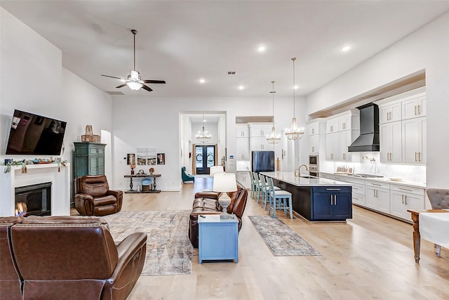 living room with light wood finished floors, recessed lighting, visible vents, a glass covered fireplace, and ceiling fan with notable chandelier