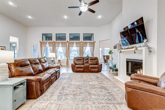 living room featuring recessed lighting, visible vents, a towering ceiling, a glass covered fireplace, and ceiling fan