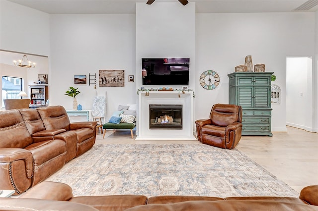 living room featuring ceiling fan with notable chandelier, visible vents, wood finished floors, and a glass covered fireplace