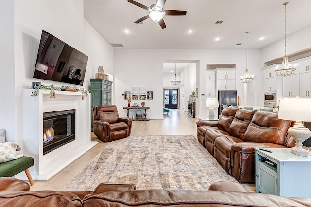 living room featuring recessed lighting, visible vents, a high ceiling, a glass covered fireplace, and ceiling fan with notable chandelier