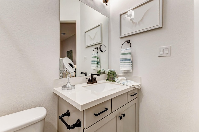 half bath with toilet, a textured wall, and vanity