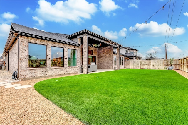 back of property featuring roof with shingles, brick siding, a lawn, ceiling fan, and a fenced backyard