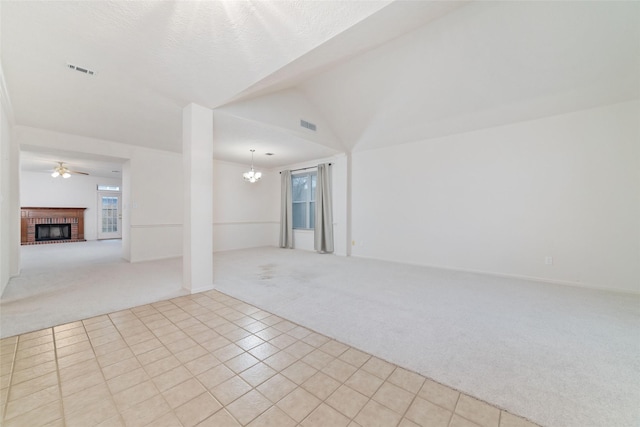 carpeted spare room featuring lofted ceiling, visible vents, a fireplace, and ceiling fan with notable chandelier