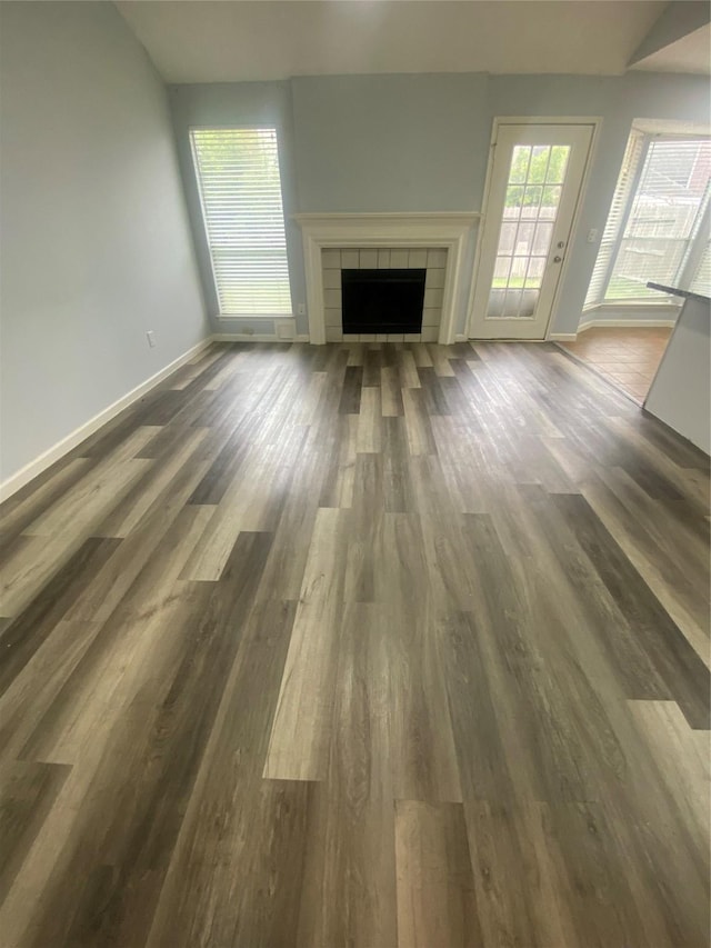 unfurnished living room with a tiled fireplace, baseboards, vaulted ceiling, and dark wood-type flooring