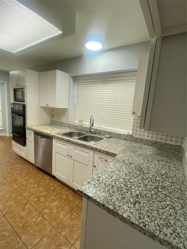 kitchen with tasteful backsplash, white cabinets, stone counters, black appliances, and a sink