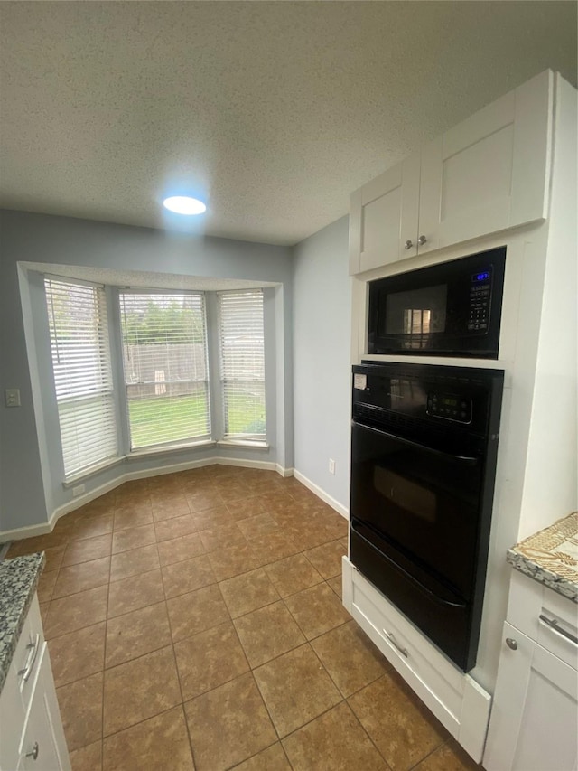 kitchen with light stone counters, black microwave, white cabinets, and plenty of natural light