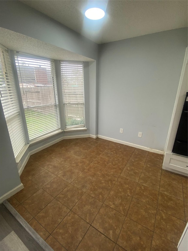 unfurnished room with a textured ceiling, dark tile patterned flooring, and baseboards