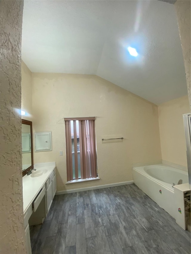 bathroom featuring lofted ceiling, vanity, wood finished floors, baseboards, and a bath