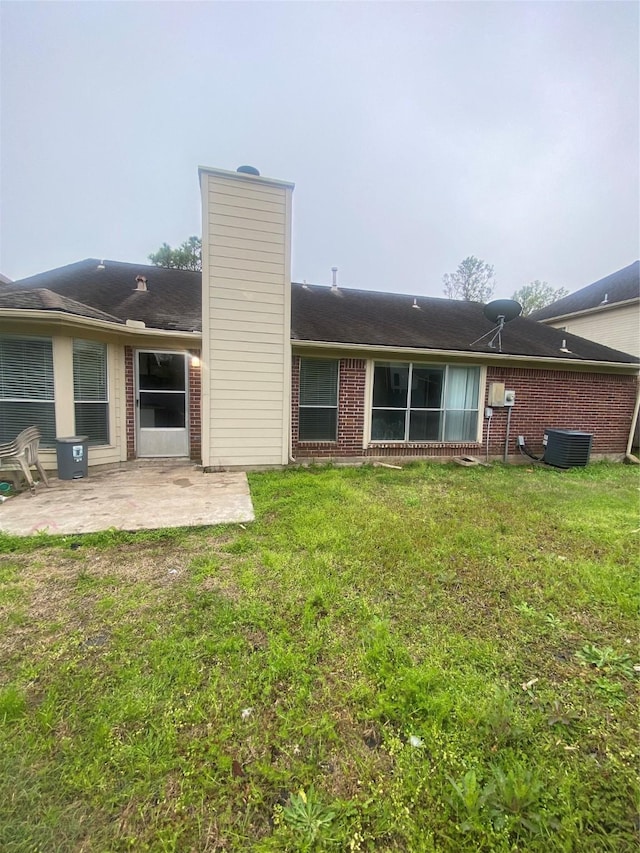 back of property with brick siding, a patio, a chimney, and a lawn