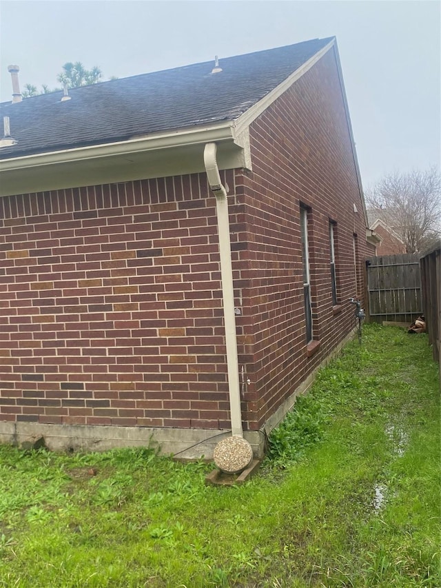 view of property exterior featuring roof with shingles, fence, a lawn, and brick siding