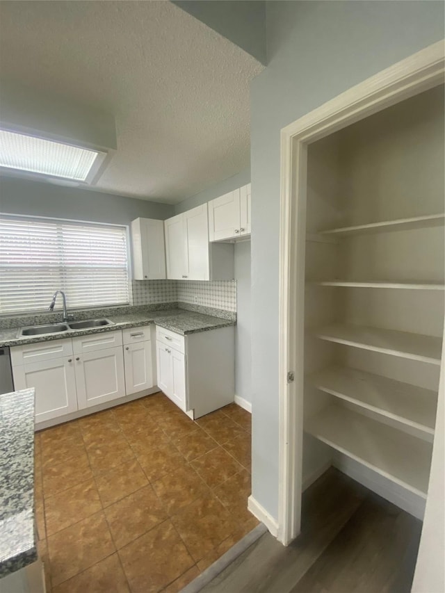 kitchen featuring a textured ceiling, white cabinets, a sink, and backsplash