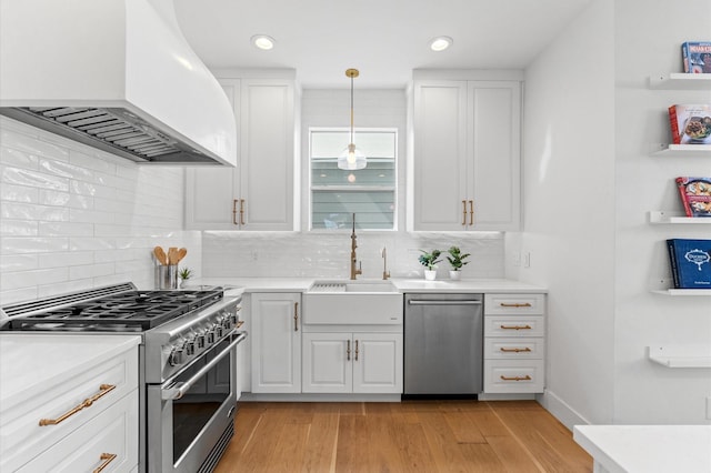 kitchen with white cabinets, light wood-style flooring, custom exhaust hood, stainless steel appliances, and a sink