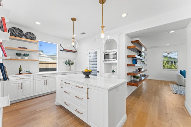 kitchen featuring open shelves, light wood finished floors, stainless steel microwave, and light countertops