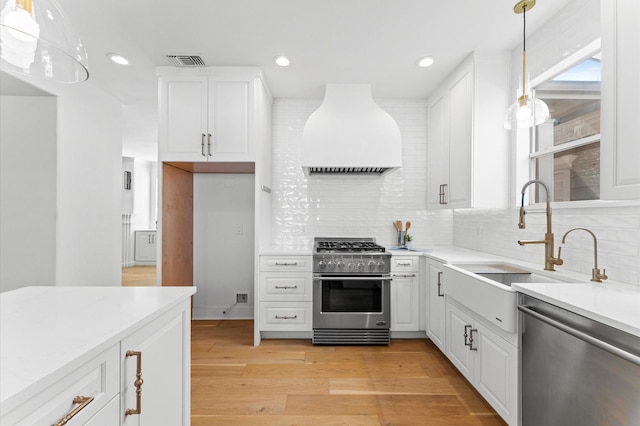 kitchen featuring light wood-style flooring, a sink, appliances with stainless steel finishes, backsplash, and custom range hood