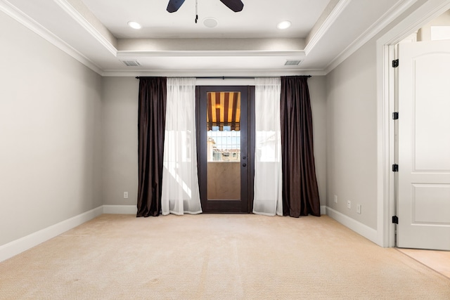 carpeted spare room with a tray ceiling, visible vents, crown molding, and baseboards