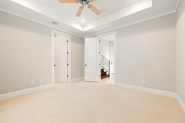 unfurnished room with light colored carpet, visible vents, baseboards, a raised ceiling, and crown molding