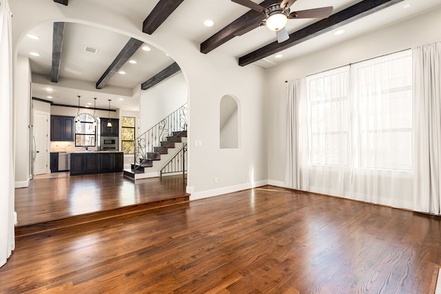 unfurnished living room with baseboards, arched walkways, visible vents, dark wood-type flooring, and stairs