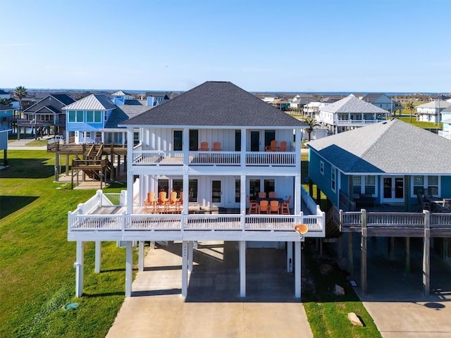 back of house with a lawn, a balcony, a residential view, roof with shingles, and a carport