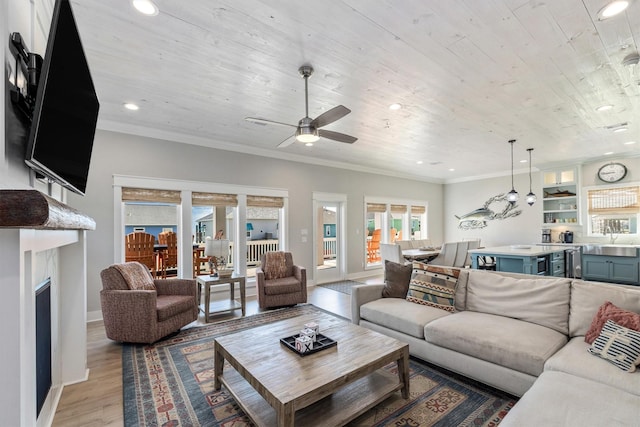 living area featuring light wood-style flooring, a ceiling fan, ornamental molding, and a fireplace