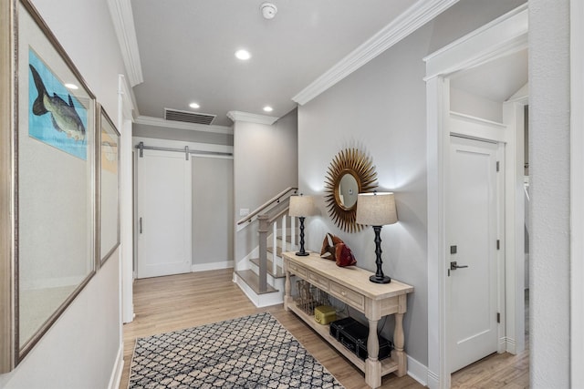 hallway featuring light wood-type flooring, visible vents, ornamental molding, a barn door, and baseboards