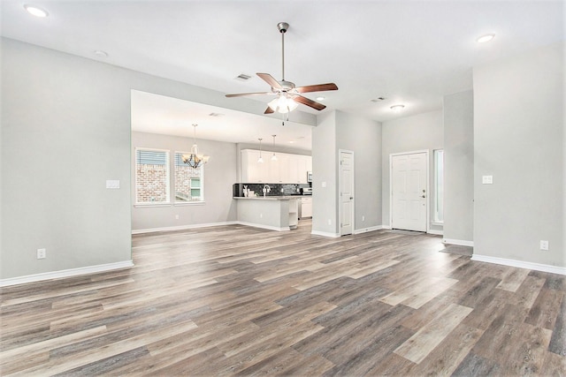 unfurnished living room featuring wood finished floors, visible vents, baseboards, and ceiling fan with notable chandelier