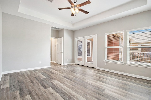 spare room featuring french doors, a tray ceiling, wood finished floors, and baseboards