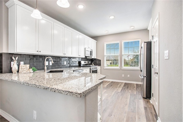 kitchen with stainless steel appliances, a peninsula, a sink, white cabinetry, and backsplash