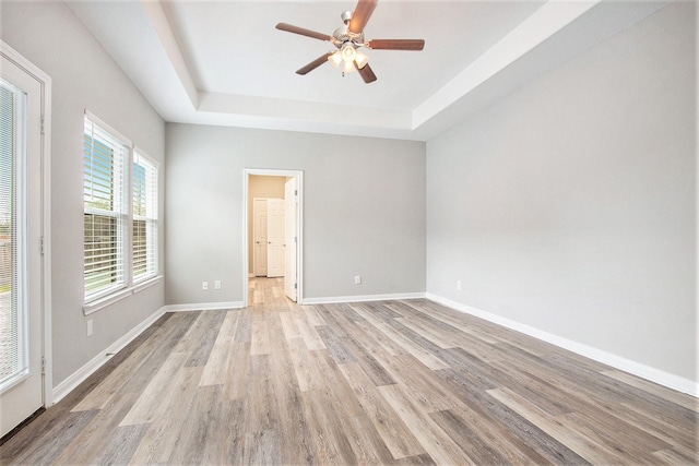 unfurnished room featuring a raised ceiling, baseboards, ceiling fan, and light wood finished floors