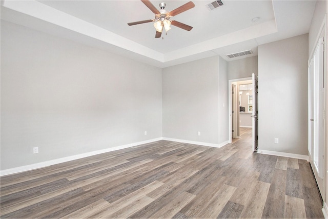 spare room with visible vents, a tray ceiling, and wood finished floors