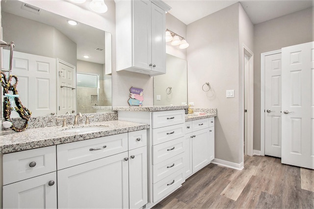 bathroom featuring visible vents, tiled shower, two vanities, wood finished floors, and a sink