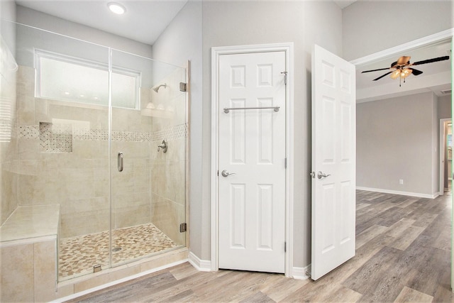 bathroom with a stall shower, ceiling fan, baseboards, and wood finished floors