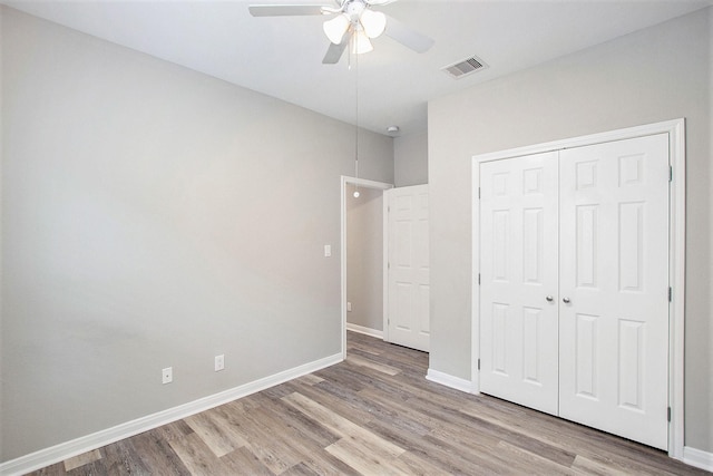 unfurnished bedroom with a closet, visible vents, baseboards, and wood finished floors