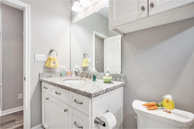 half bathroom with baseboards, a textured wall, toilet, wood finished floors, and vanity